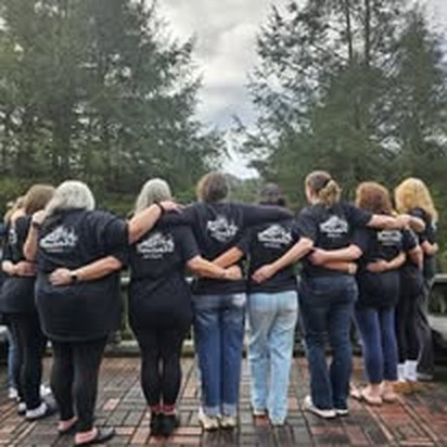 Women of the program standing in a circle with arms linked, wearing Bee Courageous shirts
